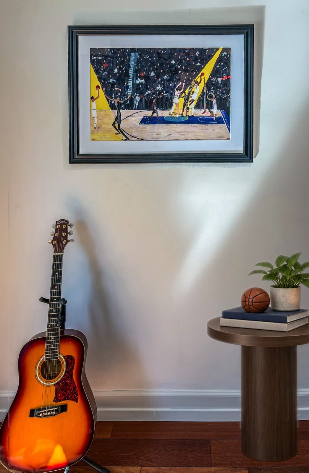 “IT’S GOOD! IT’S GOOD! IT’S GOOD!” print framed in dark wood above a guitar and side table